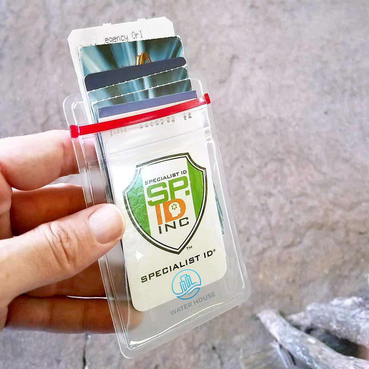 A hand holds a transparent cardholder, showcasing Custom Heavy Duty Vinyl Vertical Badge Holder w/ Resealable Zip Top (1815-1110) that includes an ID card labeled "Specialist ID SF Inc" with a shield emblem and another card partially visible behind it.