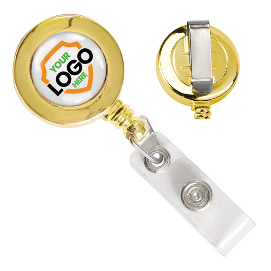 A Silver or Gold Custom Printed Retractable Badge Reels With Belt Clip - Upload Your Logo with a gold-colored finish, featuring a clip on the back for attaching to clothing and a transparent plastic snap for securing a badge. The front displays a circular area for boosting brand awareness with space for a full-color graphic logo, labeled "YOUR LOGO HERE" in green and black text.