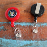 Two Custom Printed Retractable Badge Reels With Belt Clip - Personalize with Your Brand Logo rest on a wooden surface. The red reel, adorned with the US presidential seal, displays full color graphics, while the black one features a metal clip. Perfect for promoting brand awareness effortlessly.