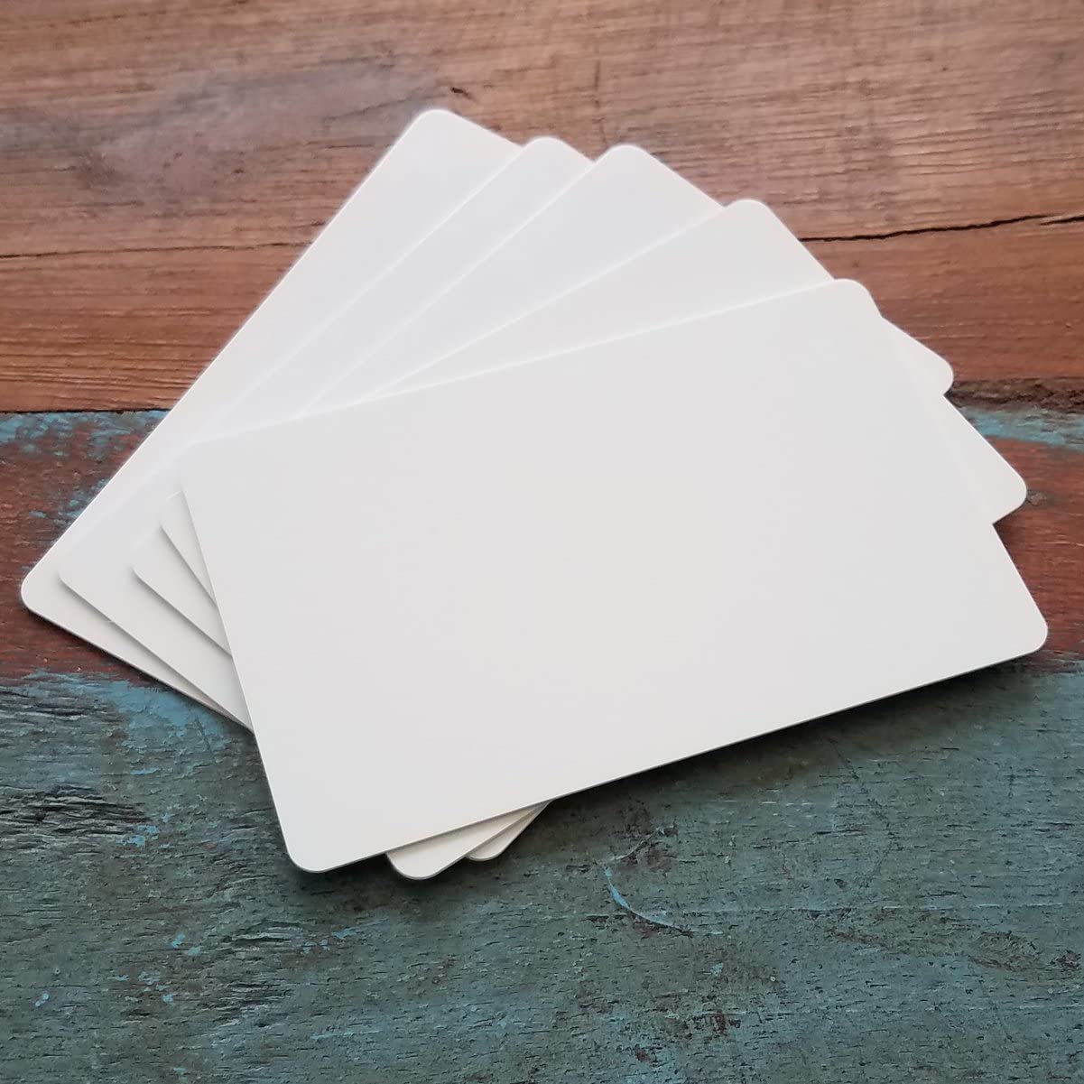 A stack of blank, white 500 Pack - Standard CR80 30mil Composite PVC/Poly Cards lies fanned out on a wooden surface—perfect for company IDs or use with ID card printers. old by Specialist ID.