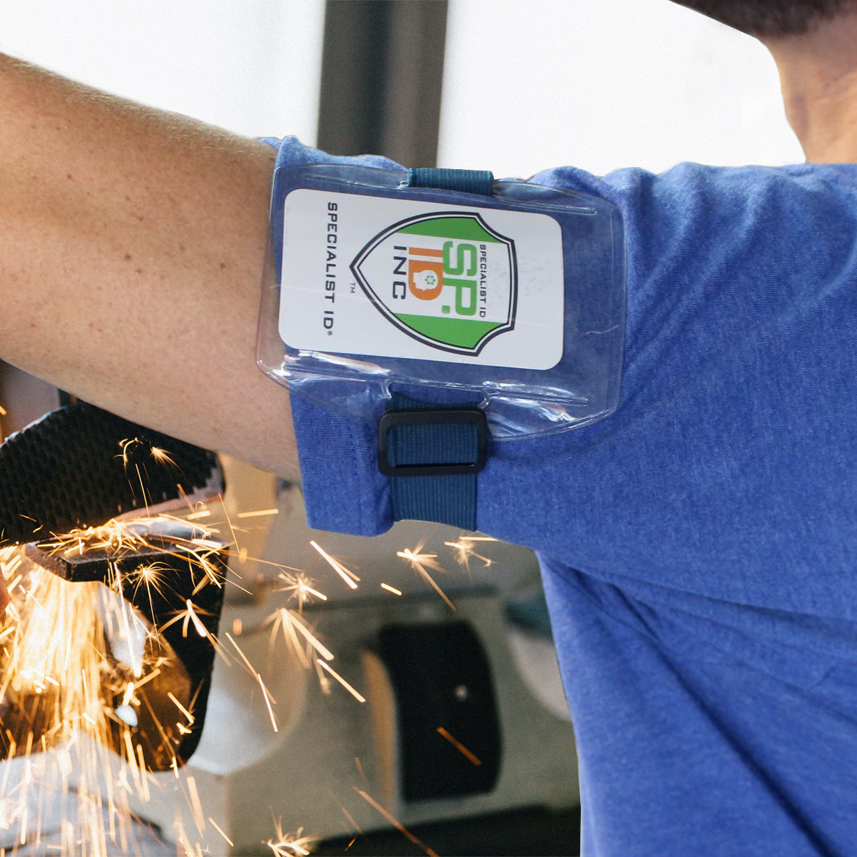 A person in a blue shirt works intently as sparks fly, the Vertical Armband ID Badge Holder (ABH-V) with an elastic band and hook and loop clasp ensuring a perfect fit amidst the action.