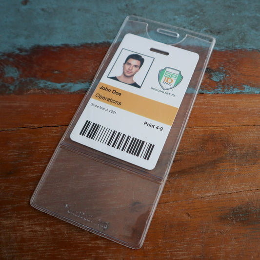A company ID badge with a photo, the name "John Doe," and "Operations" printed, issued since March 2021, placed in a Premium Vinyl Vertical BadgeBottom with Slot - Holder Only on a wooden surface.