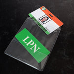 A Custom Printed BadgeBottoms® Horizontal (Badge Holder & Badge Buddy IN ONE) with a customizable title "Emily Smith" and the department "Receiving," lies next to a green card with white letters "LPN" on a black surface. The badge is neatly placed inside a sleek badge holder.
