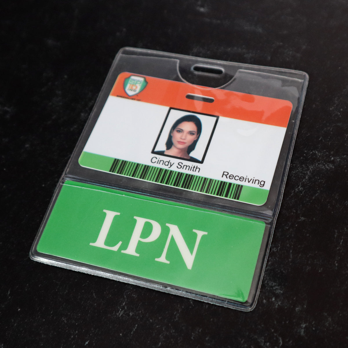 A name badge in a clear badge holder with a photo, labeled "Cindy Smith, Receiving." Below it, a green card with white letters "LPN" peeks out from the Custom Printed BadgeBottoms® Horizontal (Badge Holder & Badge Buddy IN ONE), making the setup customizable for any title.