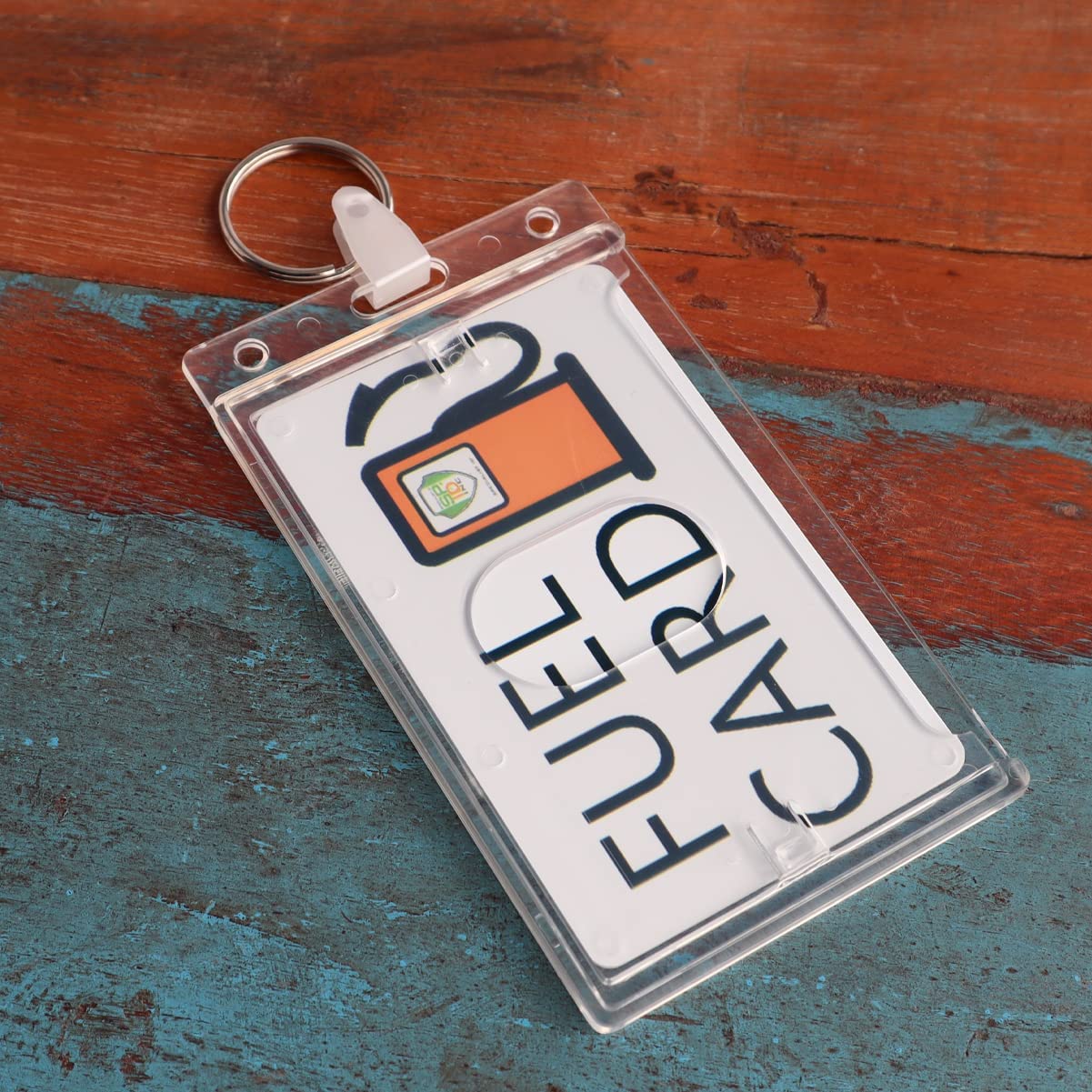 Close-up of a Custom Rigid Fuel Card Holder with Key Ring - Customize by Adding Your Logo in a clear plastic with a keyring, placed on a textured, two-toned wooden surface in blue and red.