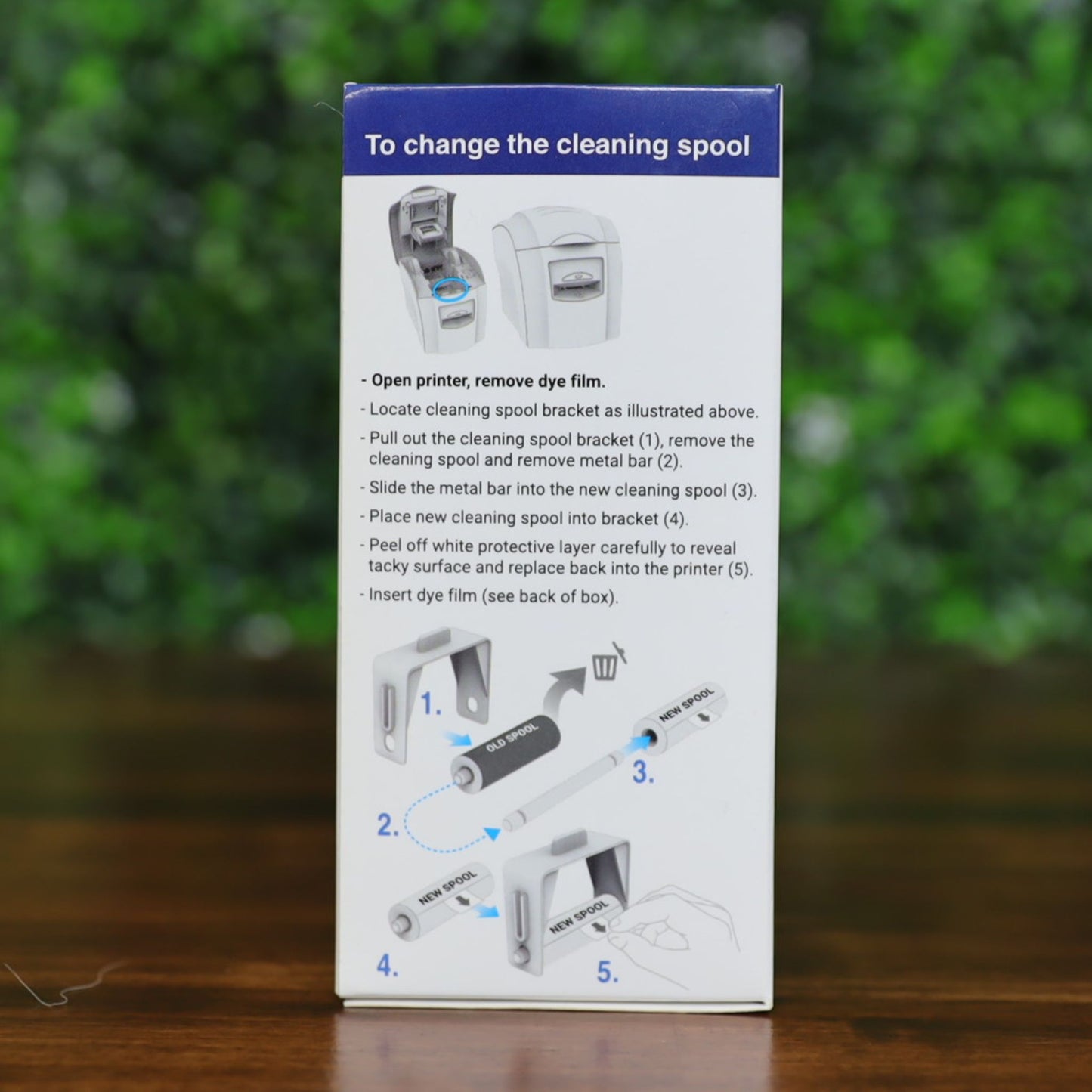 Side panel of the Magicard PR1000W monochrome ribbon box showing step-by-step cleaning spool replacement instructions. Diagram includes numbered illustrations for removing the old spool and inserting a new one using the included metal bar. Blue directional arrows guide the process. Photographed and sold by Specialist ID, an authorized Magicard dealer.