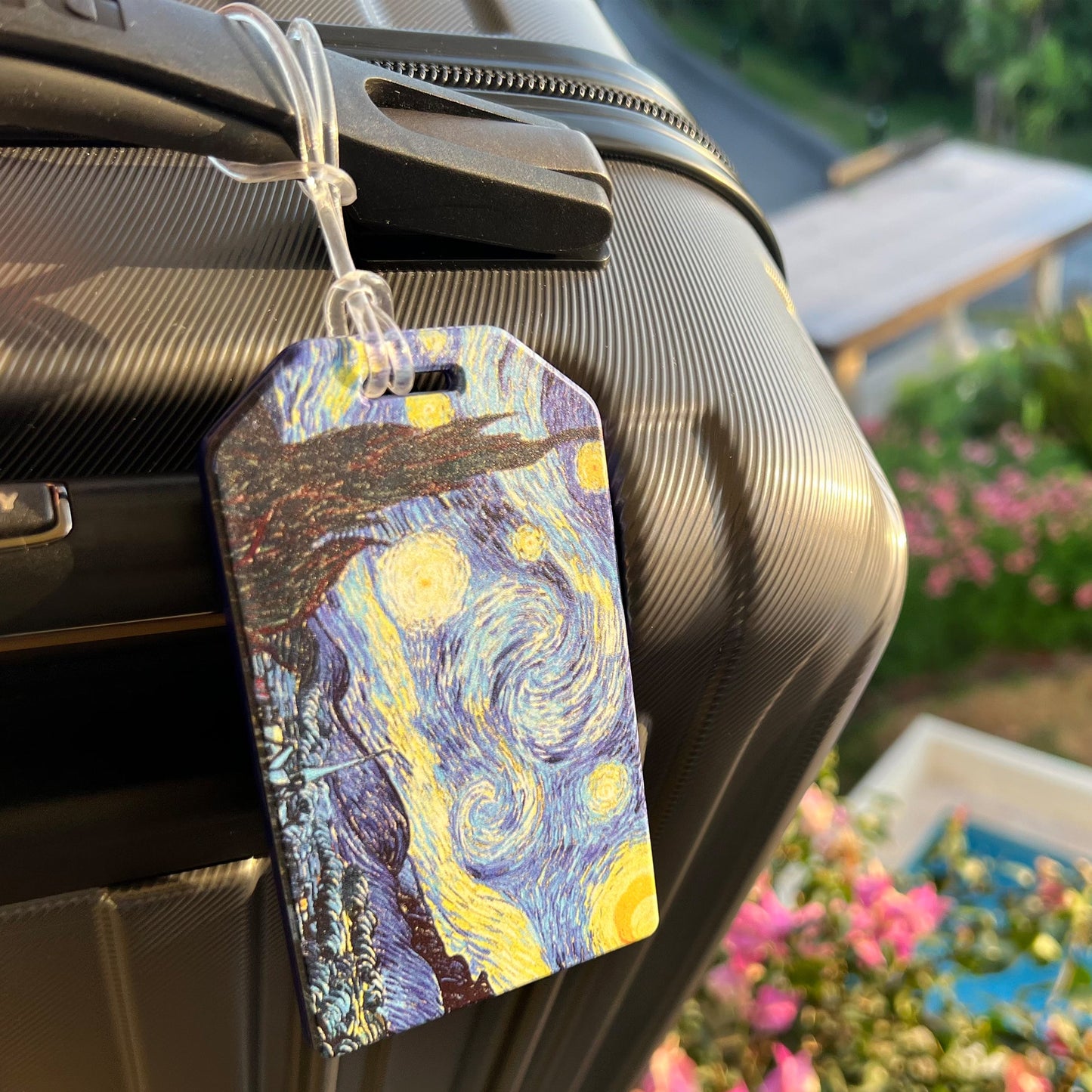 Starry Night luggage tag attached to a suitcase handle outdoors