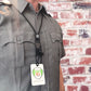 Person wearing a gray uniform shirt with dual chest pockets and a black EK Lanyard Plus with Soft End And Fused Clip (10761) by EK USA holding an identification badge that reads "Specialist ID". Background features a white and red brick wall.