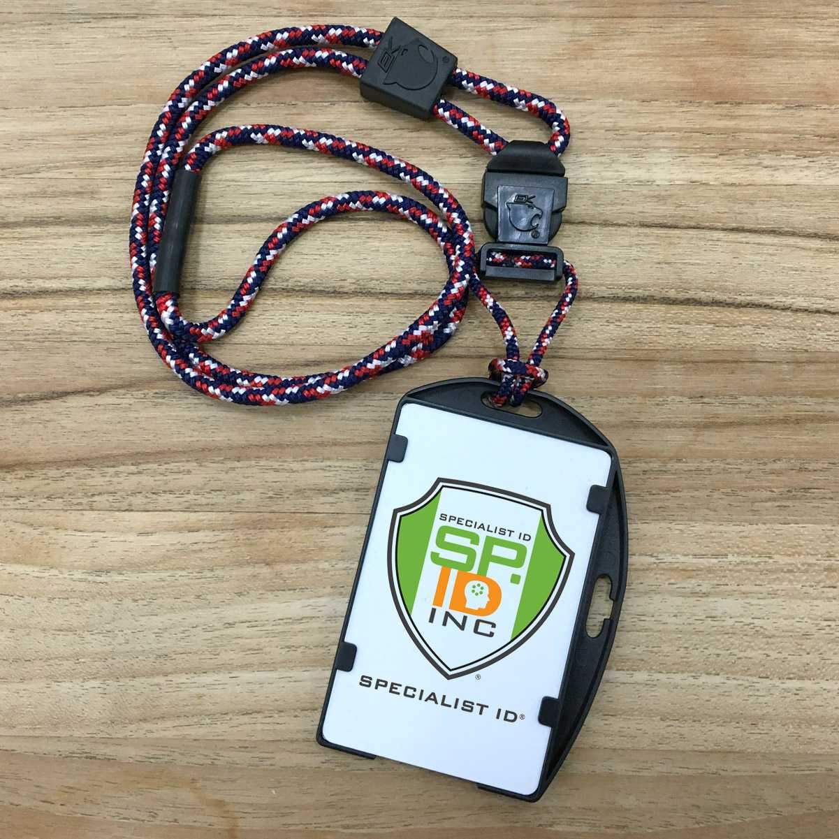 ID badge with a breakaway lanyard placed on a wooden surface. The EK USA RFID Blocking Dual Sided Badge Holder with Heavy Duty Breakaway / Quick Release Lanyard (10943) by EK USA features the Specialist ID logo and branding. The lanyard is red, white, and blue with a black clip.