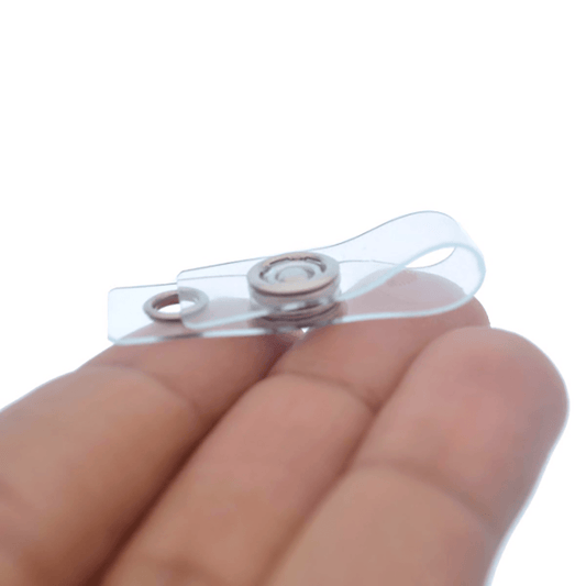 A hand holding a Key Ring to ID Badge Converting Vinyl Strap Clip 2120-1250 with a metal button at its center, perfect for attaching to an ID badge or key ring.