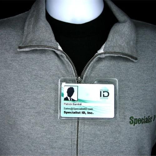 A close-up of a person wearing a gray jacket with a zippered front, displaying an ID badge labeled "Specialist ID, Inc.," and a name tag reading "Patrick Barnhill" with contact details in a Horizontal Textured Vinyl Badge Holder with Clip (P/N 1810-1000).