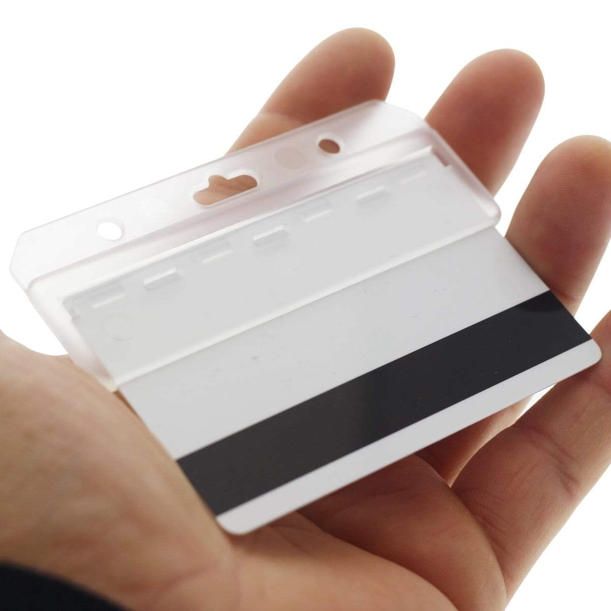 A hand holds an empty Swiple Card Holder - Rigid Horizontal Half Card Badge Holder - Leaves Mag Stripe Exposed for Easy Swiping (1840-8000) with a visible black magnetic stripe. The holder, which is ideal for access control cards, has two punched holes for attaching a lanyard.