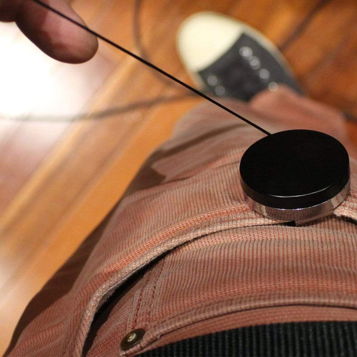 A person attached a Black Chrome Heavy Duty Badge Reel with Belt Clip (2120-3300) to their pants pocket while standing on a wooden floor. Only part of their hand and pants are visible.