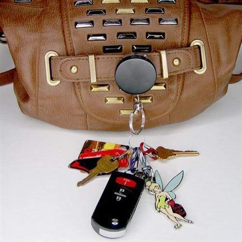 A keychain with car keys, house keys, a grocery store card, and a Tinker Bell figurine hangs from a brown handbag using a Heavy Duty Badge Reel with Chain & Belt Clip - Strong All Metal Retractable Keychain for Keys and Badges (2120-3325).