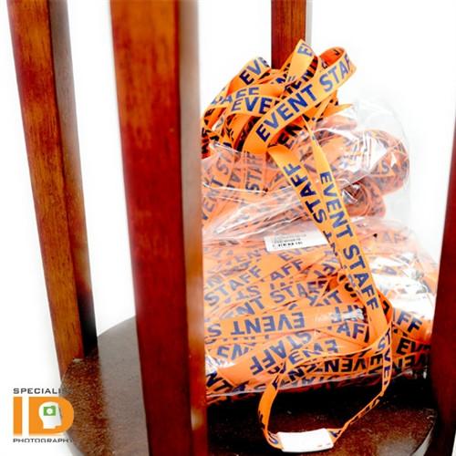 A bundle of orange "Event Staff" Breakaway Flat Lanyard With Swivel Hook (2138-5200) is placed on the wooden seat of a chair.