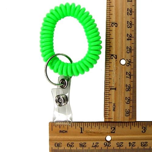 A green Wrist Coil Key Chain with ID Strap Clip (2140-620X) is placed next to a wooden ruler, making it the ideal key accessory for organizing your essentials.