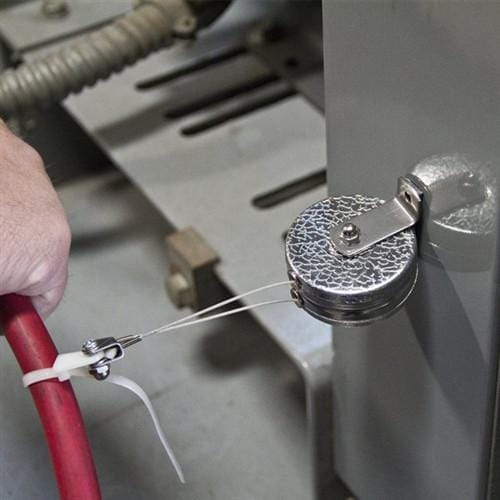 A hand is connecting a red grounding wire to a metallic grounding point on a machine, ensuring proper electrical safety with the aid of a Key-Bak #481LS-Twin Industrial Dual Retractable Reel with 48" Steel Cable.