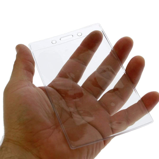 A hand holding a 3 1/4" X 5" Clear Premium Vinyl Vertical Extra Large ID Badge Holder (P/N 506-35625) with two pre-punched holes at the top.