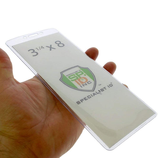 A hand holds a 3X8 Clear Vinyl Vertical Extra Large Badge Holder (506-35875) displaying an insert with "3 1/4 x 8" dimensions, the logo of Specialist ID, Inc., and a convenient lanyard attachment.