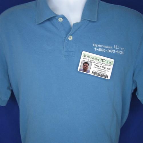 A close-up of a person wearing a blue polo shirt with a company logo and phone number, along with an ID badge displaying a photo and barcode affixed to the shirt using a Magnetic ID Badge Holder Sticky Back (P/N 5730-3000).
