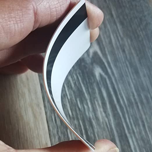 A close-up photo of a hand holding a flexed piece of white paper with Standard CR80 30mil Cards w/ HiCo Mag Stripe. The background features a wooden surface.