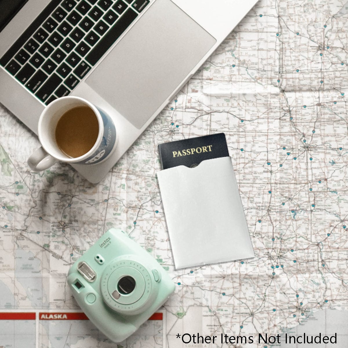 Flat lay of a laptop, coffee cup, SkimSAFE Shielded RFID Passport Protection Sleeve 153036 (AH-225), and mint green instant camera on a map. An asterisk note reads "*Other Items Not Included.