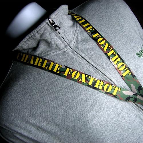 Close-up of a gray hoodie worn by a mannequin, attached to a Charlie Foxtrot Camouflage Breakaway Military Lanyard with the text "CHARLIE FOXTROT" in yellow letters. The lanyard includes a breakaway feature for added safety.