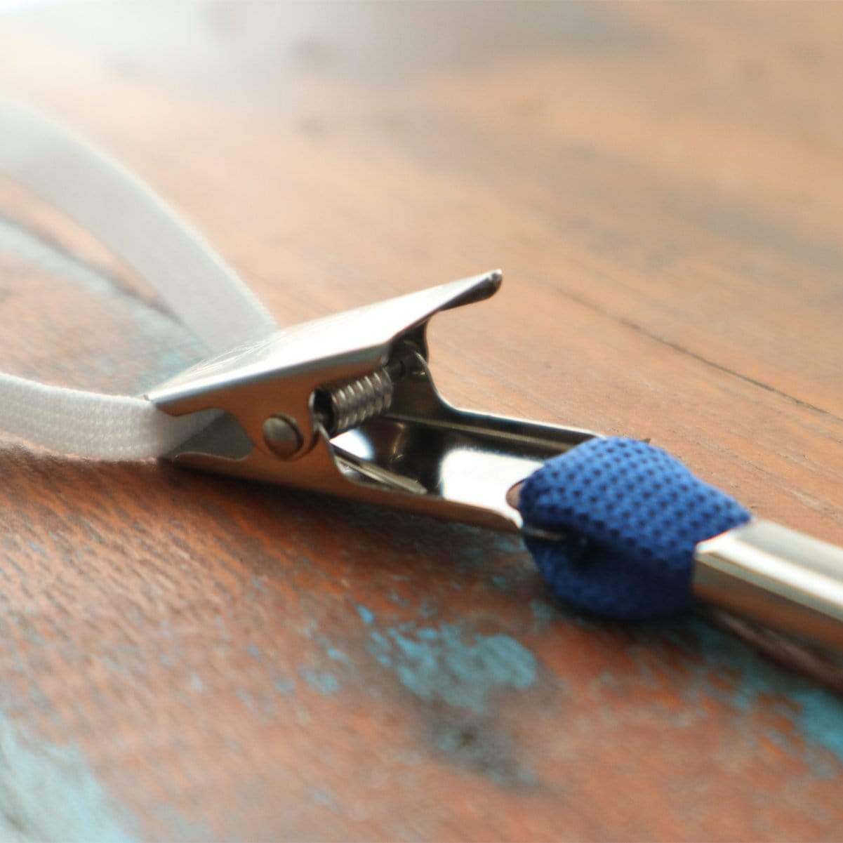 A close-up image of a metal alligator clip attached to a 5 Pack Double Ended Lanyards with Bulldog Clips - Comfortable Premium Economy Neck Strap Badge Holder for Events, set on a wooden surface.