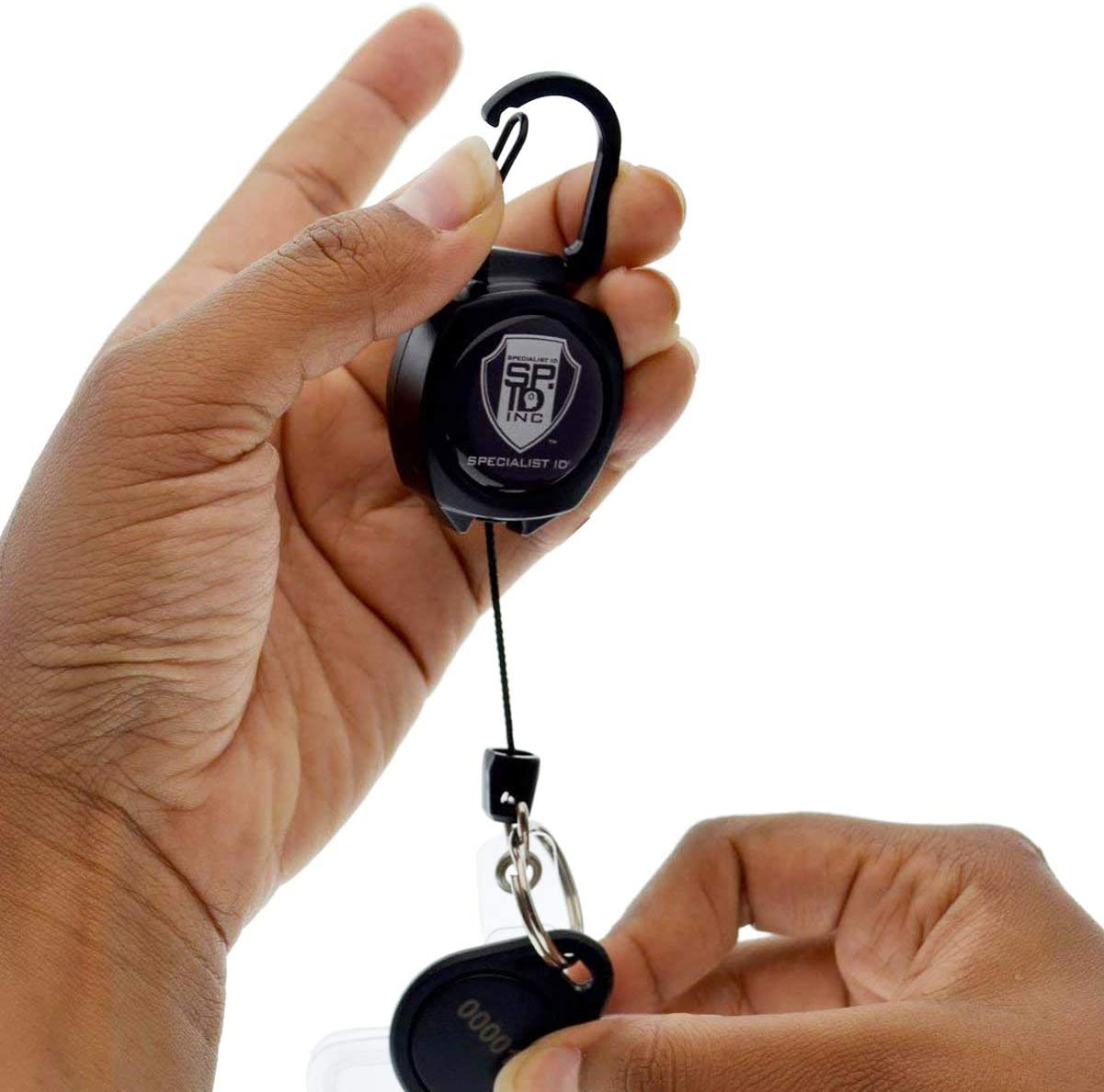 A person holds an SPID Key-Bak SIDEKICK Heavy Duty Retractable Carabiner Badge Reel with ID Holder Strap & Keychain in one hand, while inserting a key into the other end of the ID badge reel with the other hand.