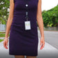 A person wearing a sleeveless purple dress and a Top Loading THREE ID Card Badge Holder with Heavy Duty Lanyard w/ Detachable Metal Clip and Key Ring by Specialist ID, walking on a sidewalk with trees and a fence in the background.