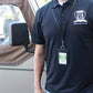 A person wearing a black polo shirt with a Specialist ID Inc. logo and a Heavy Duty Union Made Genuine Leather ID Badge Holder Wallet & Lanyard (SPID-9590-BLACK) stands next to a vehicle with a side mirror.