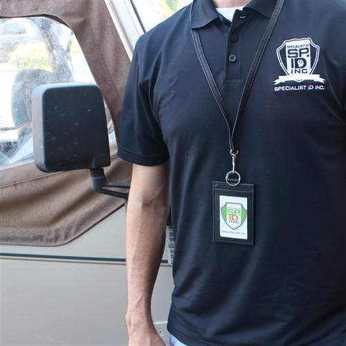 A person wearing a black polo shirt with a Specialist ID Inc. logo and a Heavy Duty Union Made Genuine Leather ID Badge Holder Wallet & Lanyard (SPID-9590-BLACK) stands next to a vehicle with a side mirror.