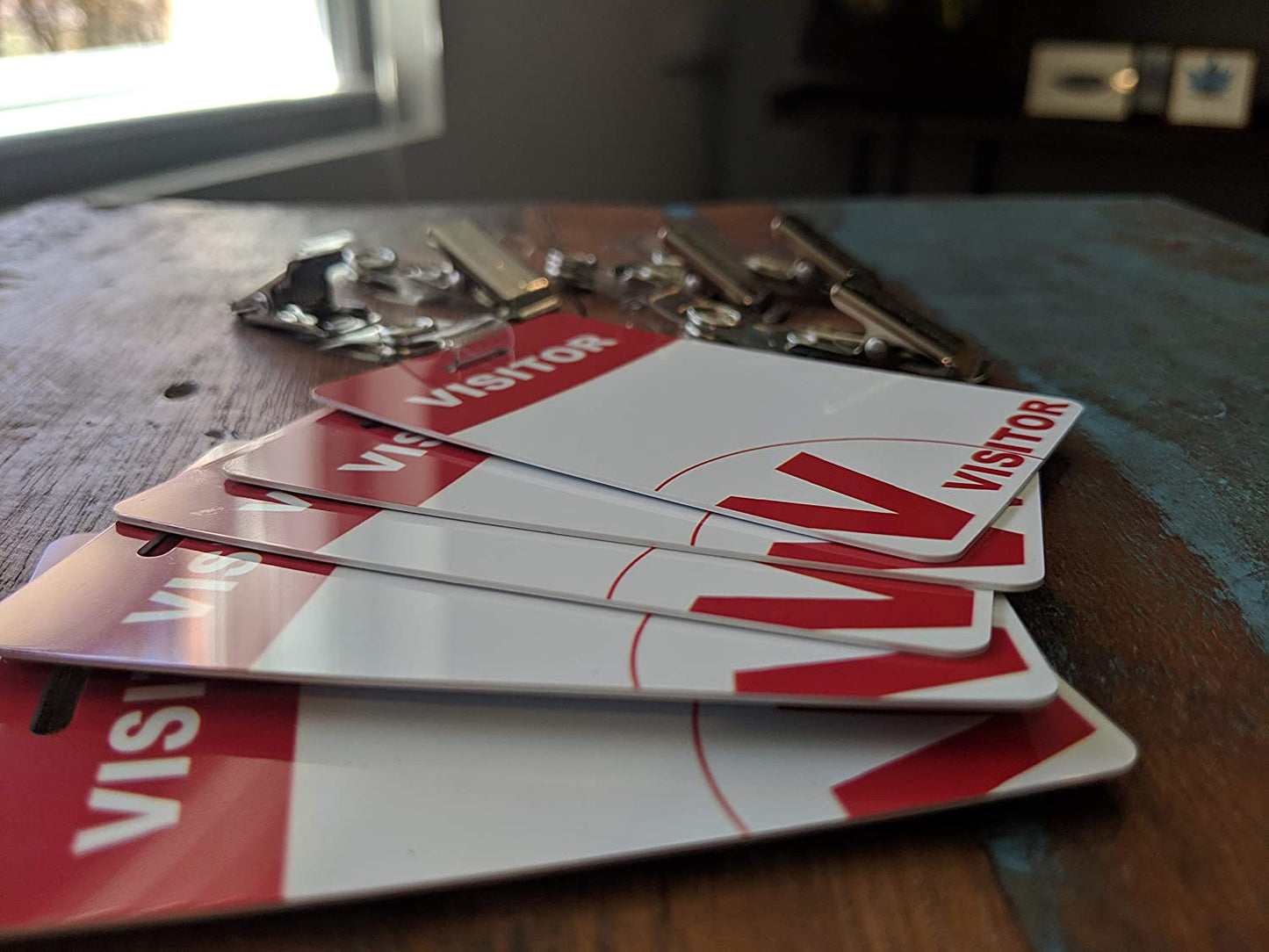 Reusable Visitor Passes with Clothing Friendly Badge Clip are placed on a wooden table near a window, alongside a dry-erase marker for easy updating.