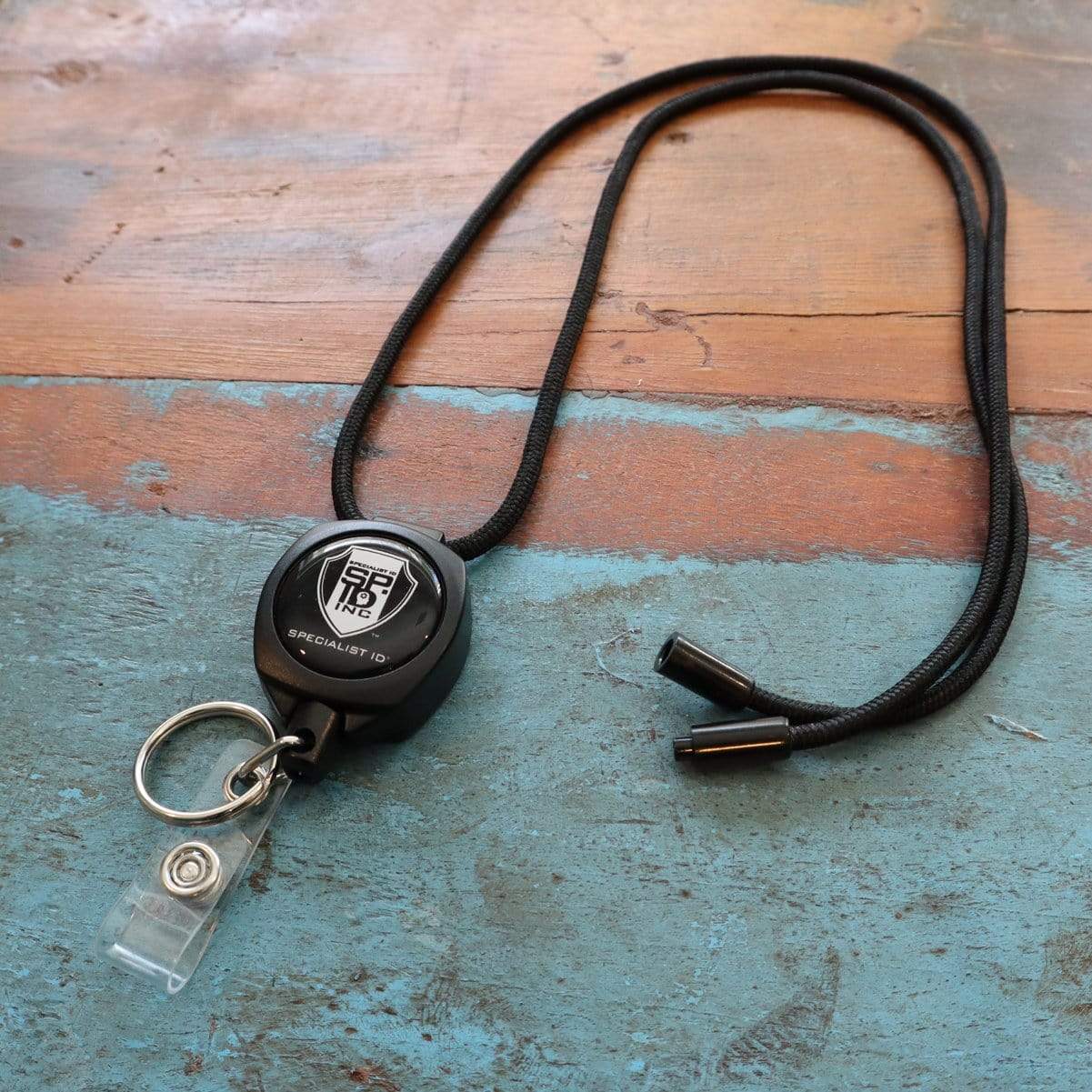 SPID Key-Bak SIDEKICK Heavy Duty Badge Reel Lanyard Combo with ID Holder Strap Clip & Key Ring (SPID-9980) with a durable breakaway lanyard and a clip, branded with the logo "SEIKO," lying on a weathered wooden surface with a blue painted area.