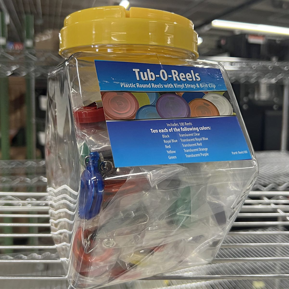 A clear plastic jar with a yellow lid labeled "Assorted Badge Reels TUB-O-REELS" containing assorted badge reels in various colors, displayed on a metal shelf.