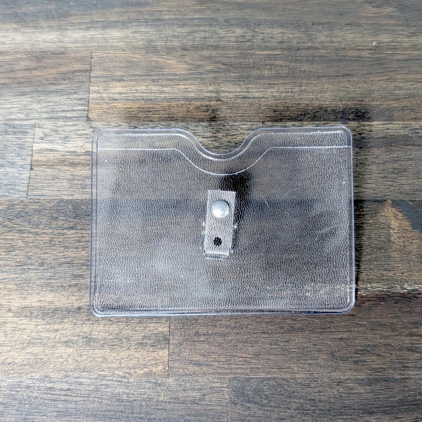 The Horizontal Textured Vinyl Badge Holder with Clip (P/N 1810-1000) is shown on a wooden surface, ideal for keeping your ID badge secure and visible.