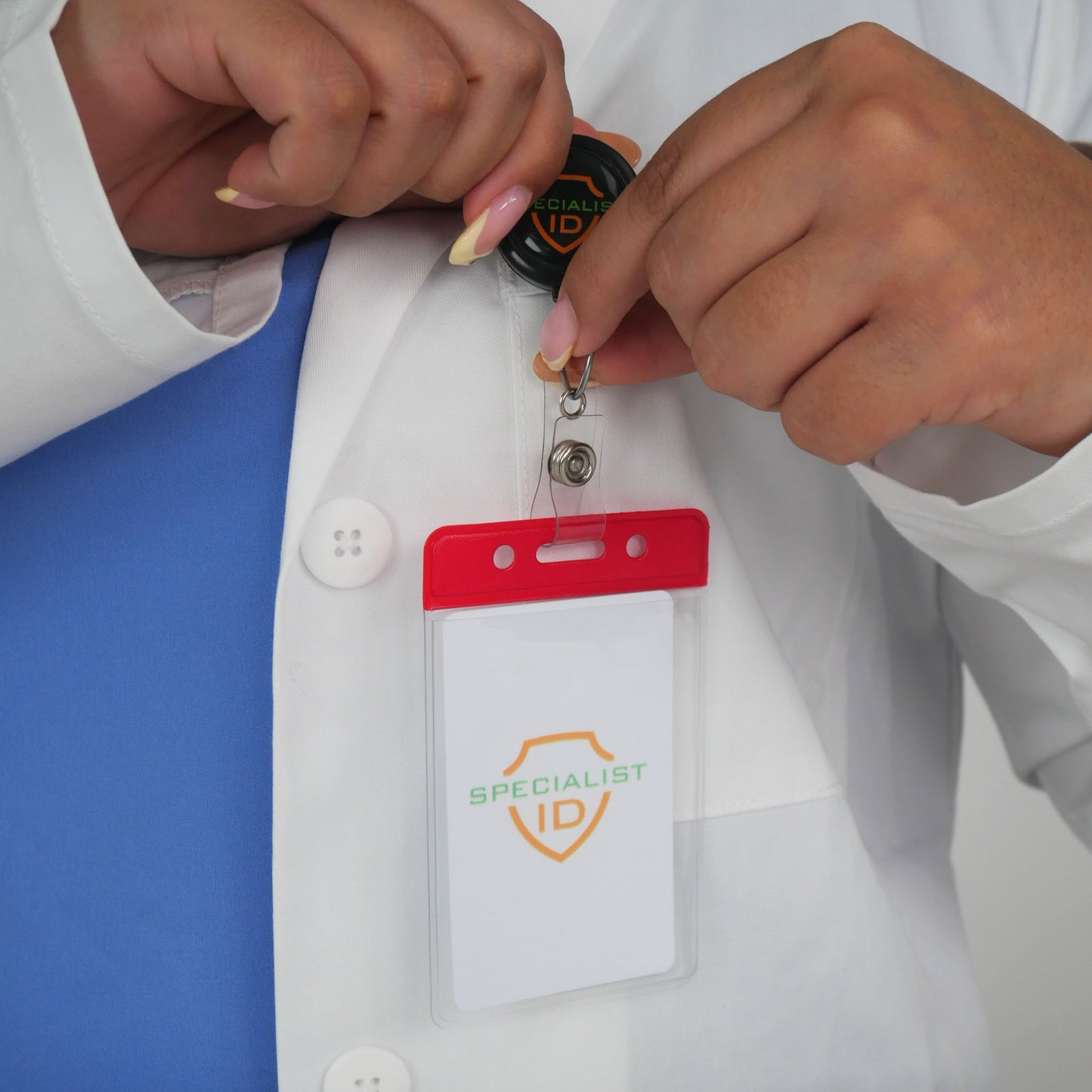 A person in a lab coat clips a Vertical Vinyl Badge Holder with Color Bar, Standard ID Badge Size (1820-105X) onto their shirt.