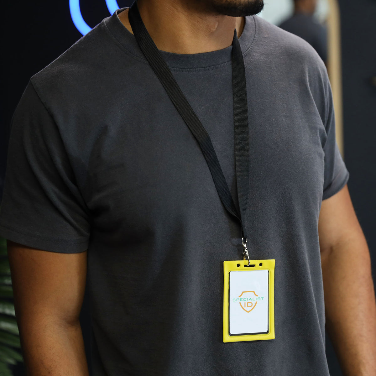 Person wearing a plain dark gray t-shirt and a lanyard with a Vertical Vinyl Color Frame Badge Holder (P/N 1820-300x) around their neck.