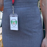 A person wearing a gray dress with an ID badge hanging on a lanyard. The ID badge, secured in a Custom Clear Vertical Permanent Locking Plastic Card Holder - Add Your Logo, displays the logo and text "Specialist ID Inc.