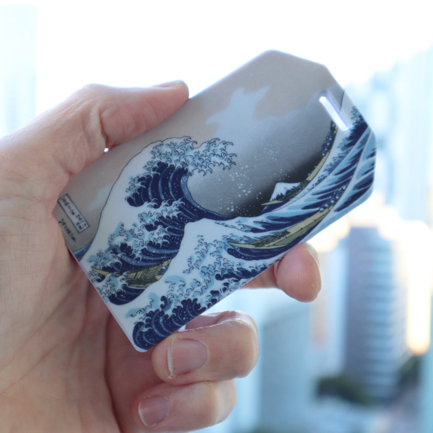 Great Wave luggage tag held in hand with clear plastic loop