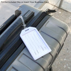 A close-up of a grey suitcase with a white Custom Rigid Plastic Luggage Tag Holders with 6" Clear Loop - Personalize with Your Logo attached. The tag includes fields for name, address, telephone, and email. Text above reads, "Fill out included slip or insert your business card.