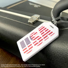 A close-up of a black suitcase with Custom Rigid Plastic Luggage Tag Holders with 6" Clear Loop - Personalize with Your Logo featuring an American flag design and the letters "USA" highlights the potential for custom luggage tags as effective promotional giveaways. The suitcase is resting on a wooden surface, emphasizing brand awareness through its distinctive tag.
