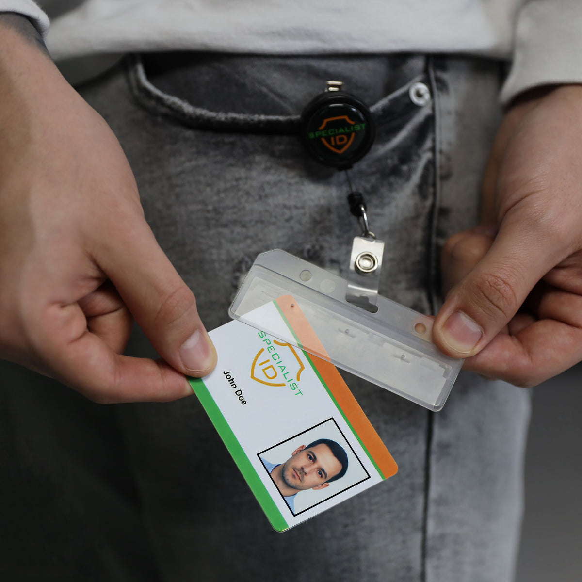 A person holds a Swipe Card Holder - Rigid Horizontal Half Card Badge Holder - Leaves Mag Stripe Exposed for Easy Swiping (1840-8000) with an ID card and retractable badge reel.