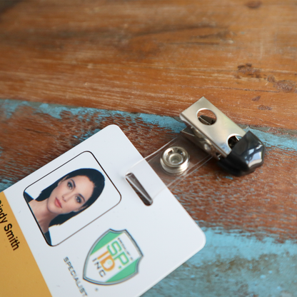 A detailed view of the Clothing Protector ID Strap Clip with Rubber Tip, 2105-3170, featuring an ID badge with a photo, all placed on a wooden surface.