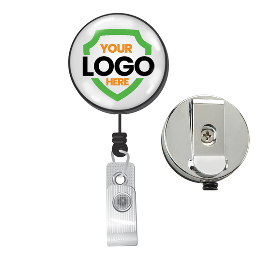 A round retractable badge holder with a clip on the back. The front displays a placeholder for a logo with the text "YOUR LOGO HERE" inside a green and orange shield, perfect for Custom Badge Reels - Heavy Duty Custom Printed Badge Reel with Belt Clip - Upload Your Logo to enhance brand visibility during promotional giveaways.