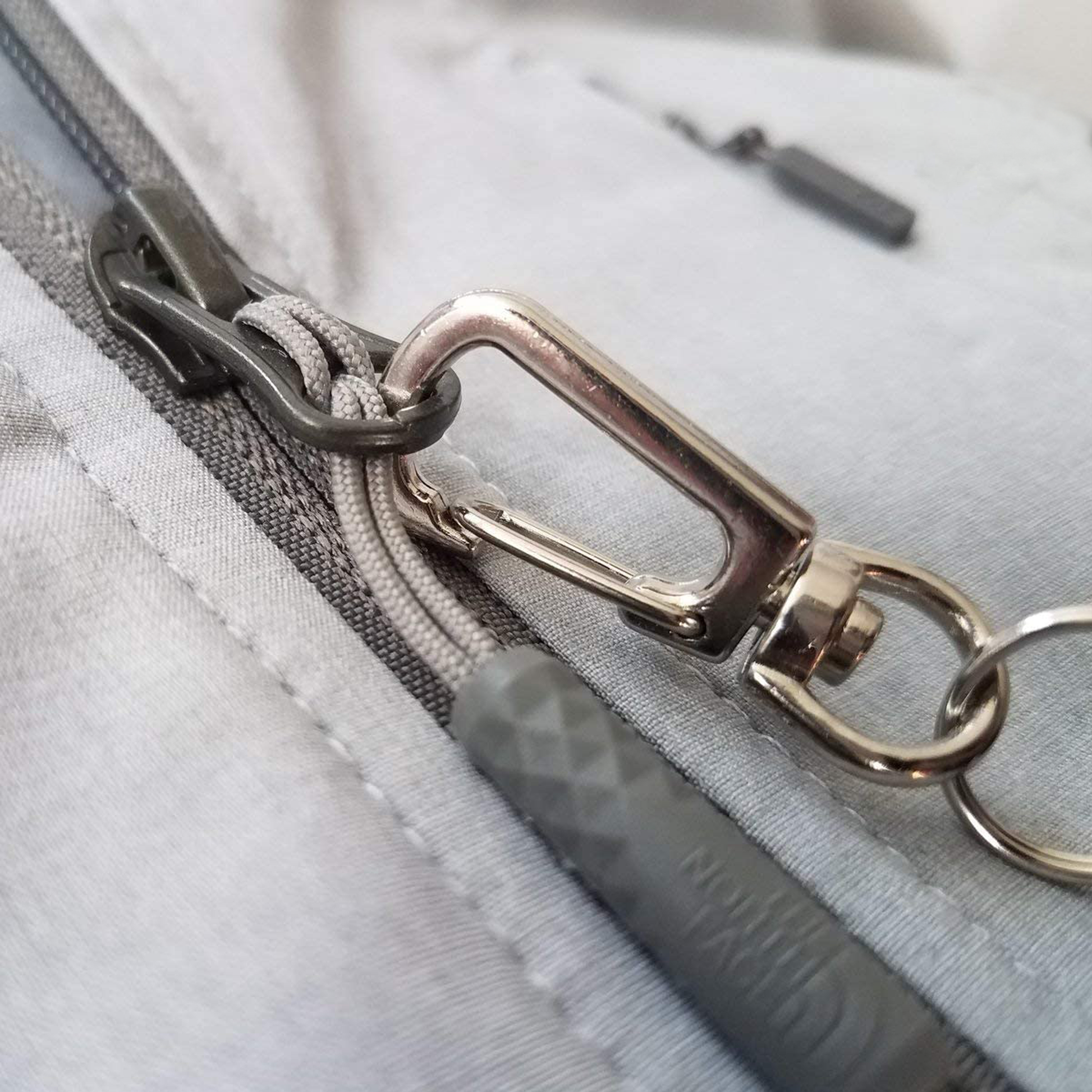 Close-up of a gray zipper with a Ski Pass Holder Retractable Heavy Duty Sport Reel (P/N 2120-4101) attached. The fabric and detail of the zipper are visible, making it an ideal ski pass holder.
