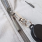 Close-up of a gray jacket zipper with a Ski Pass Holder Retractable Heavy Duty Sport Reel (P/N 2120-4101) attached to the heavy-duty zipper pull.