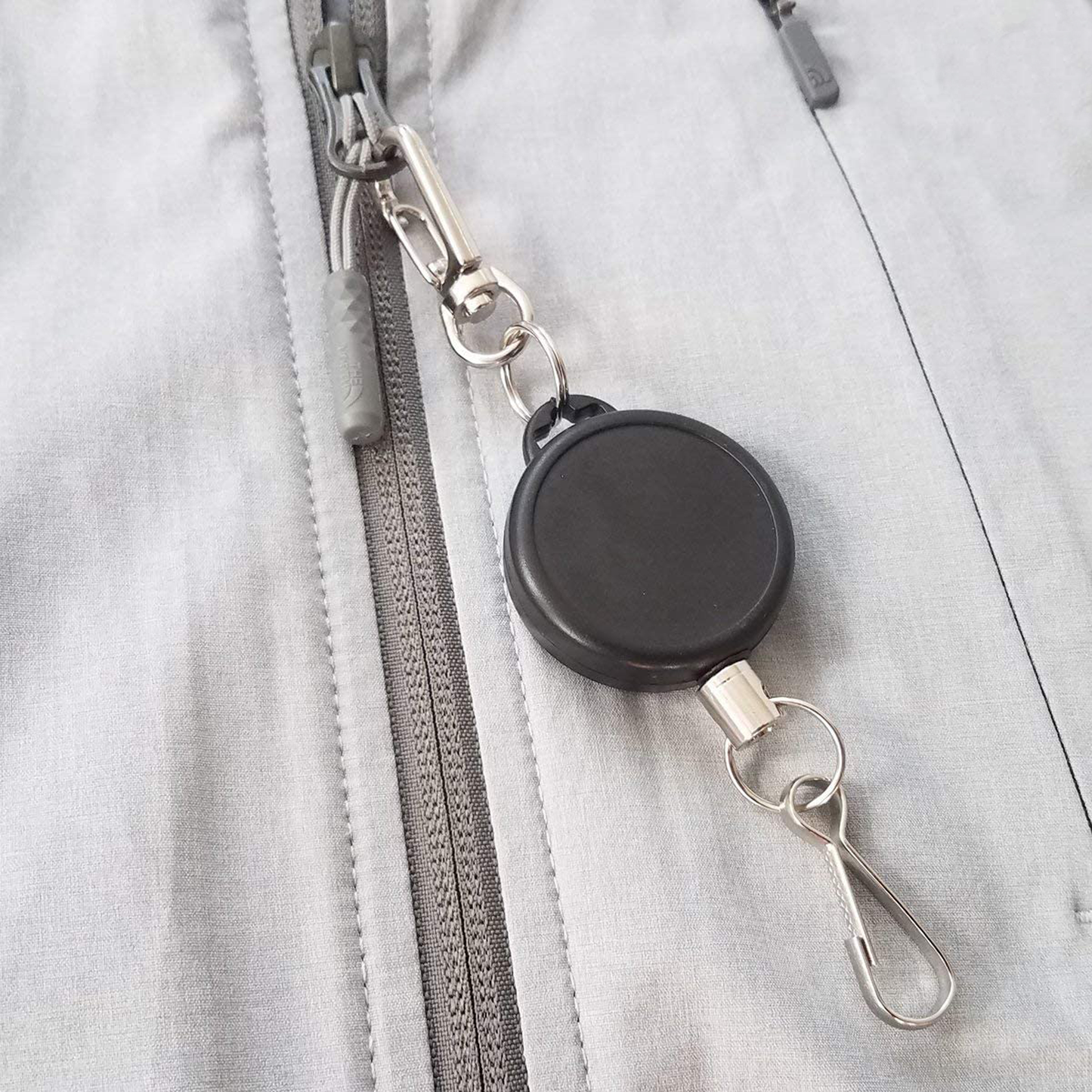 A Ski Pass Holder Retractable Heavy Duty Sport Reel (P/N 2120-4101) clipped to the zipper of a gray jacket, perfect as a ski pass holder.