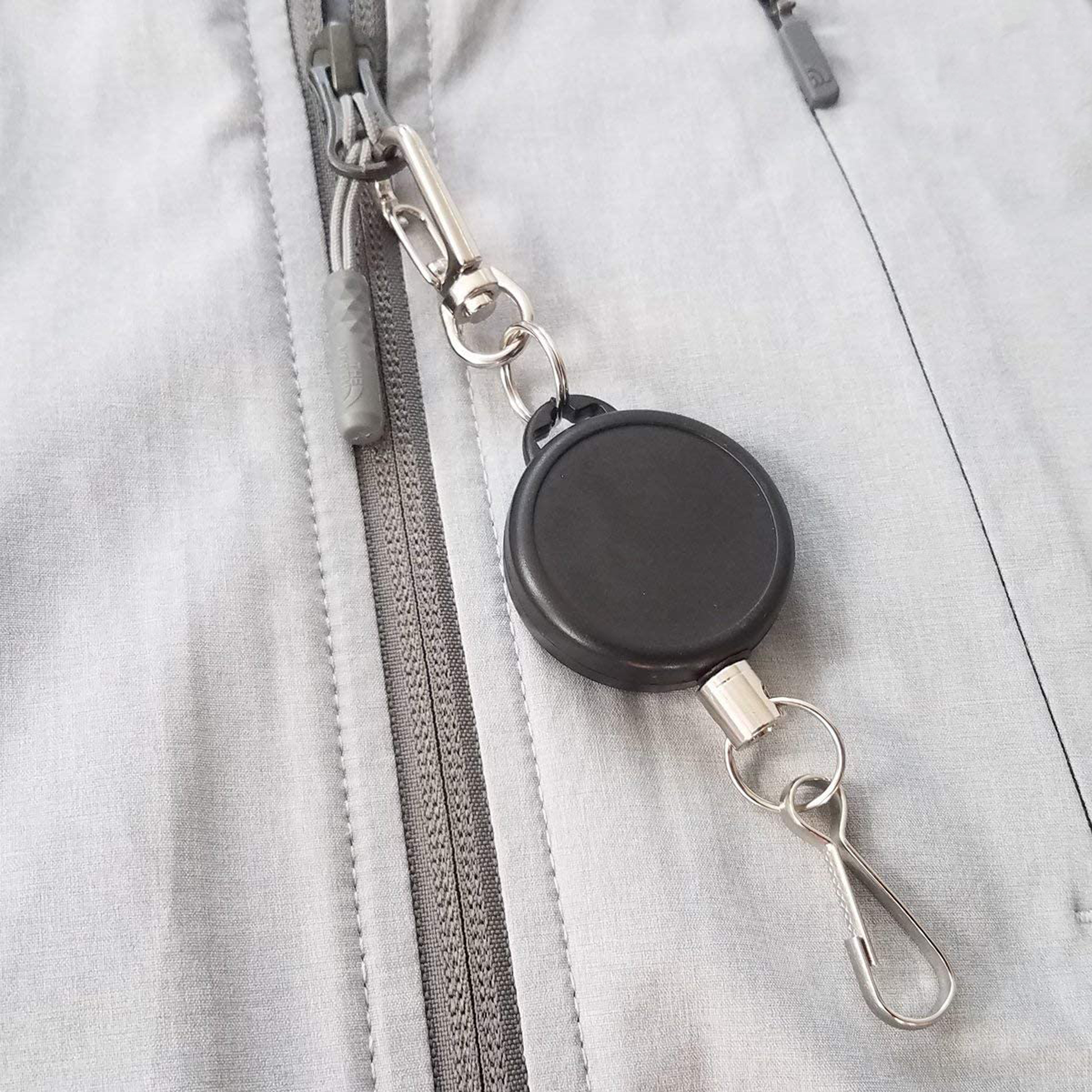 A Ski Pass Holder Retractable Heavy Duty Sport Reel (P/N 2120-4101) clipped to the zipper of a gray jacket, perfect as a ski pass holder.