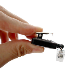 A person gently holds a sleek black Custom Square Retractable Badge Reel with Spring Clip between their fingers against a pristine white background. Sold by Specialist ID.